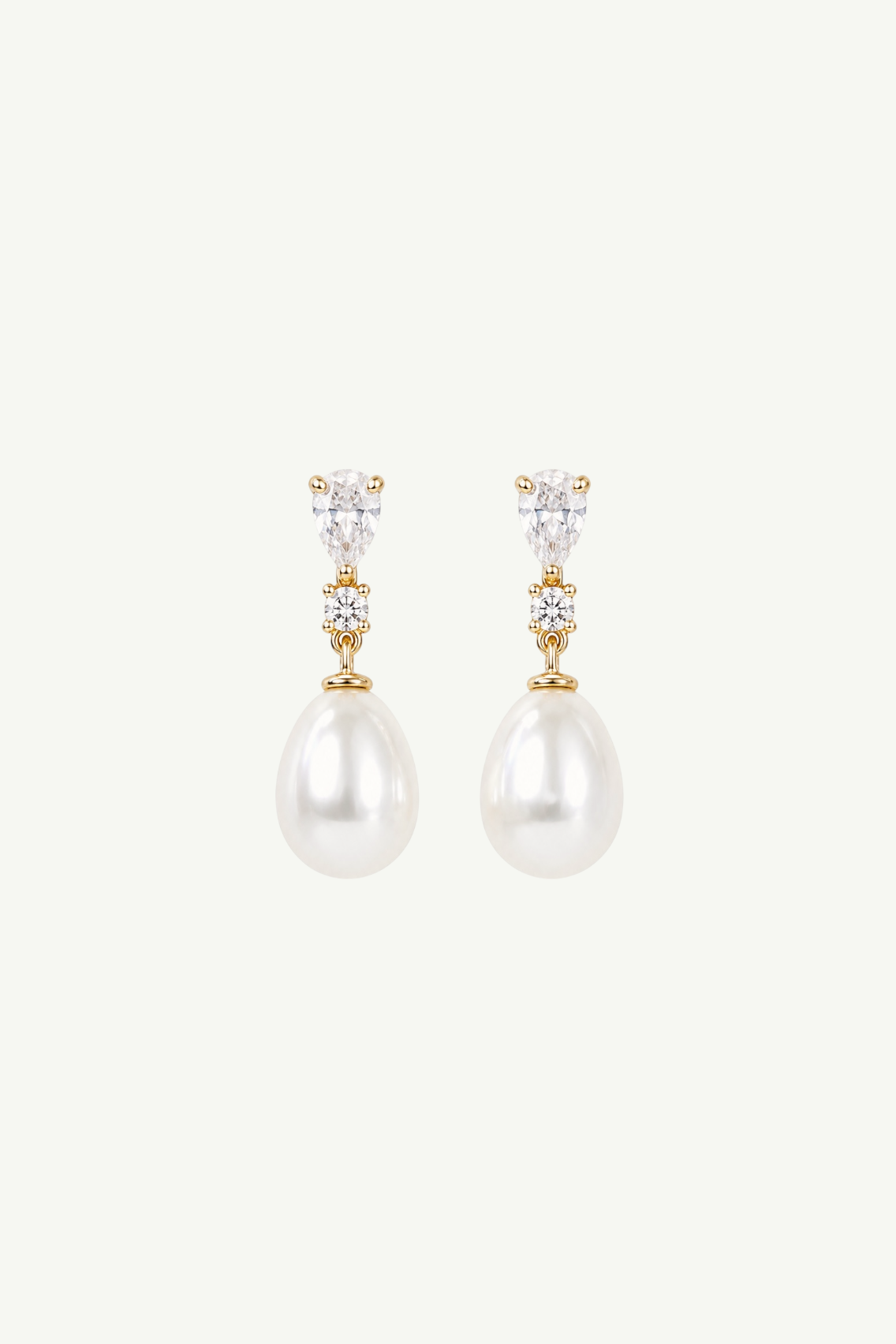 A pair of gold drop earrings featuring a small cluster of clear stones above a large white pearl, set against a plain off-white background.