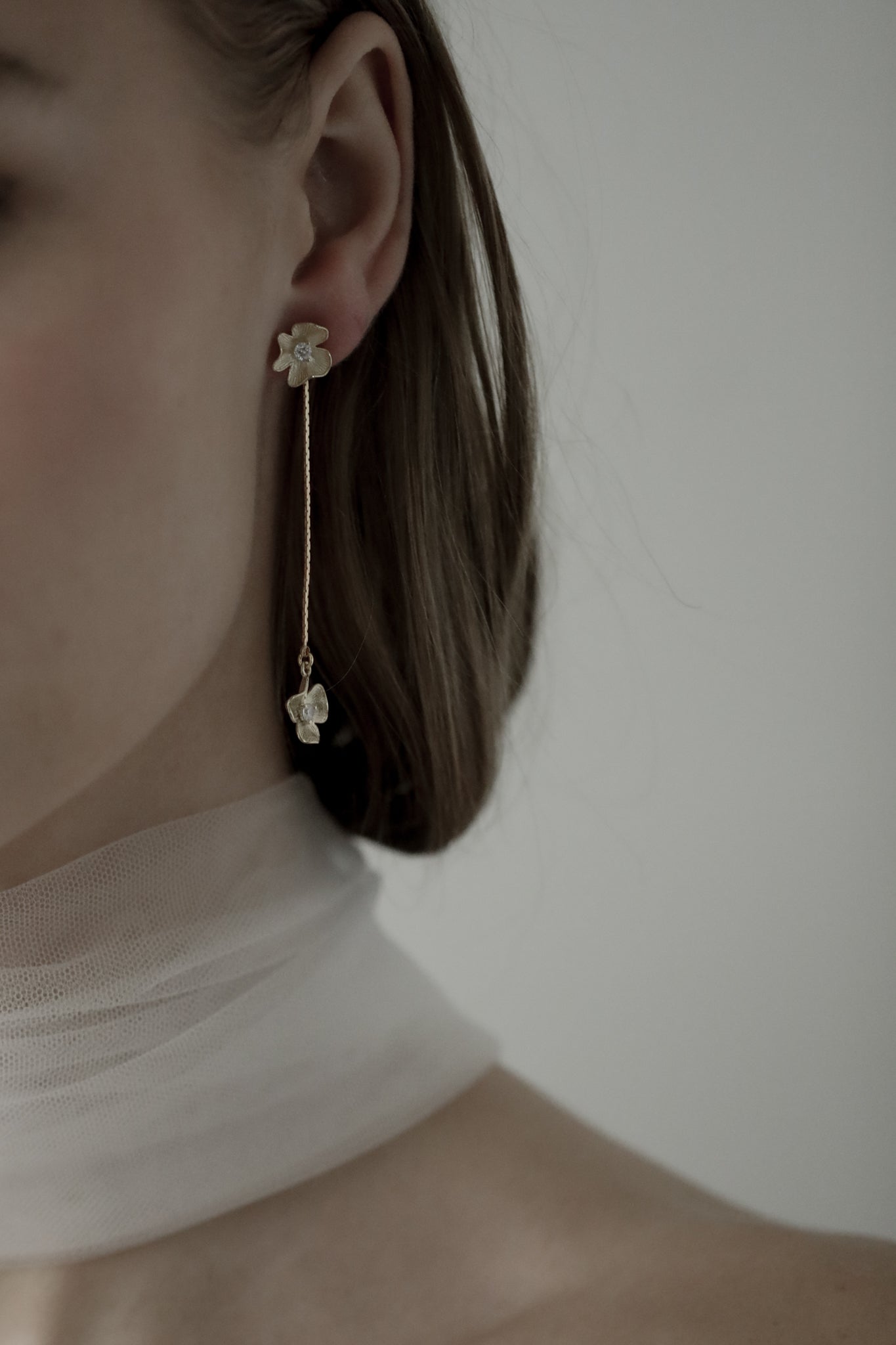 Close up image of gold plated floral strand earring with rhinestone accents worn by brunette bride wearing a silk bridal scarf
