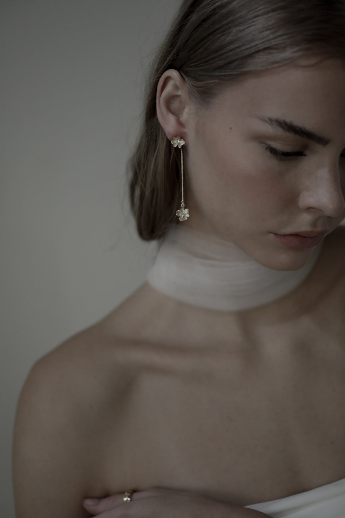 Side view from shoulder up of gold plated floral strand earring with rhinestone accents worn by brunette bride wearing a silk bridal scarf