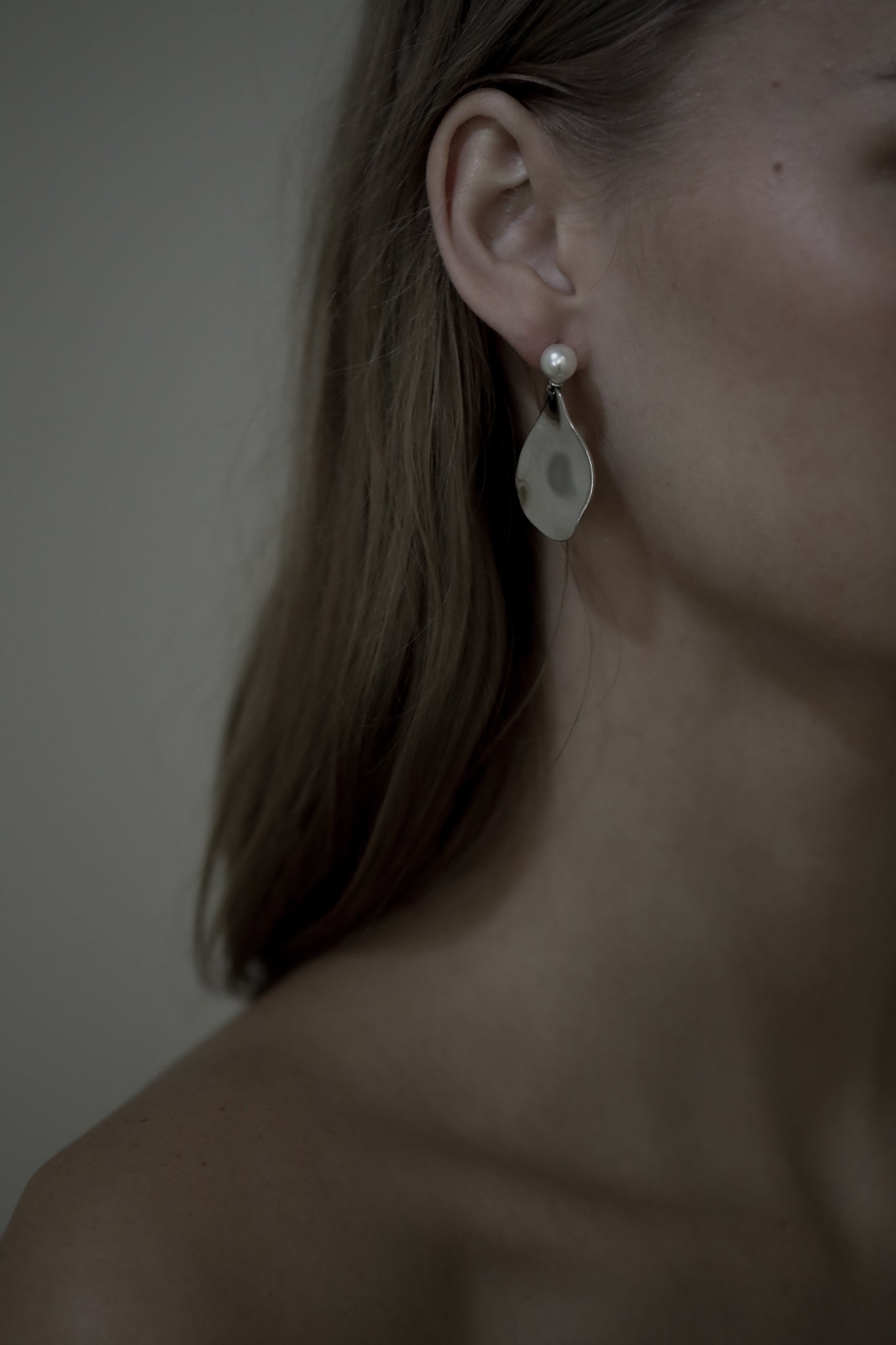 Close up image of brunette bride wearing irregular sculptural gold metallic earrings with a pearl stud accent
