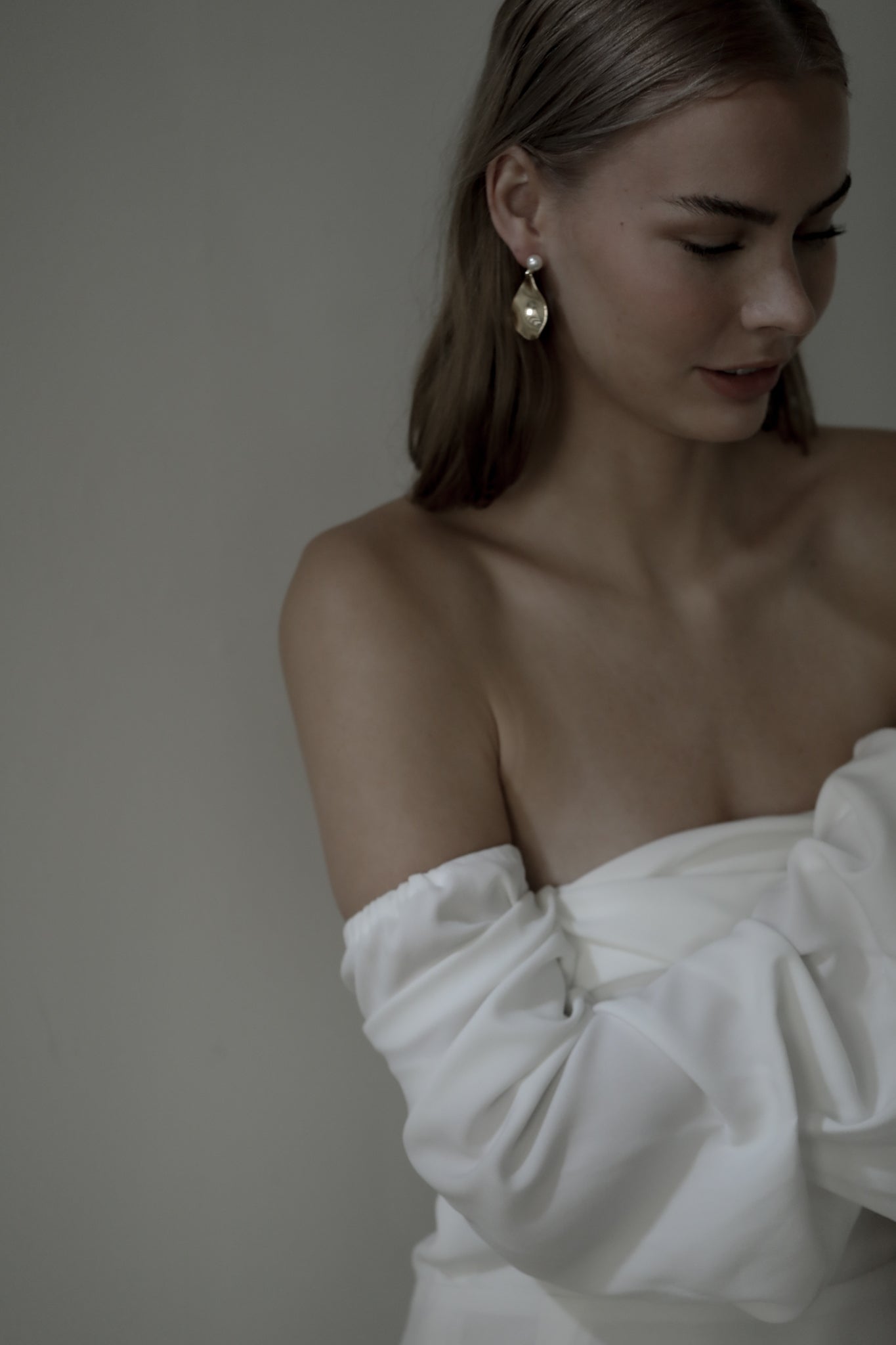 Brunette bride wearing strapless bridal gown paired with gold sculptural drop earrings that feature a pearl stud accent