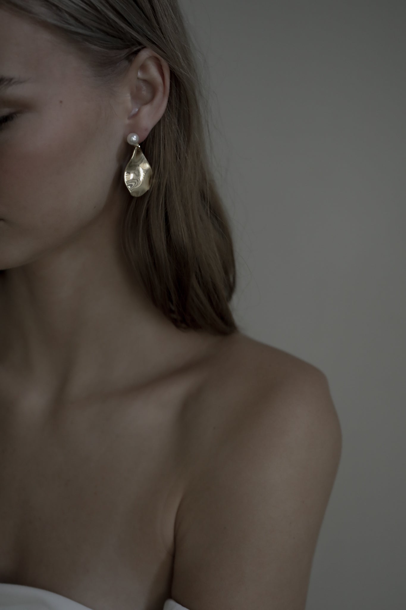 Brunette bride wearing strapless wedding dress paired with gold irregular drop earrings that feature a pearl stud accent