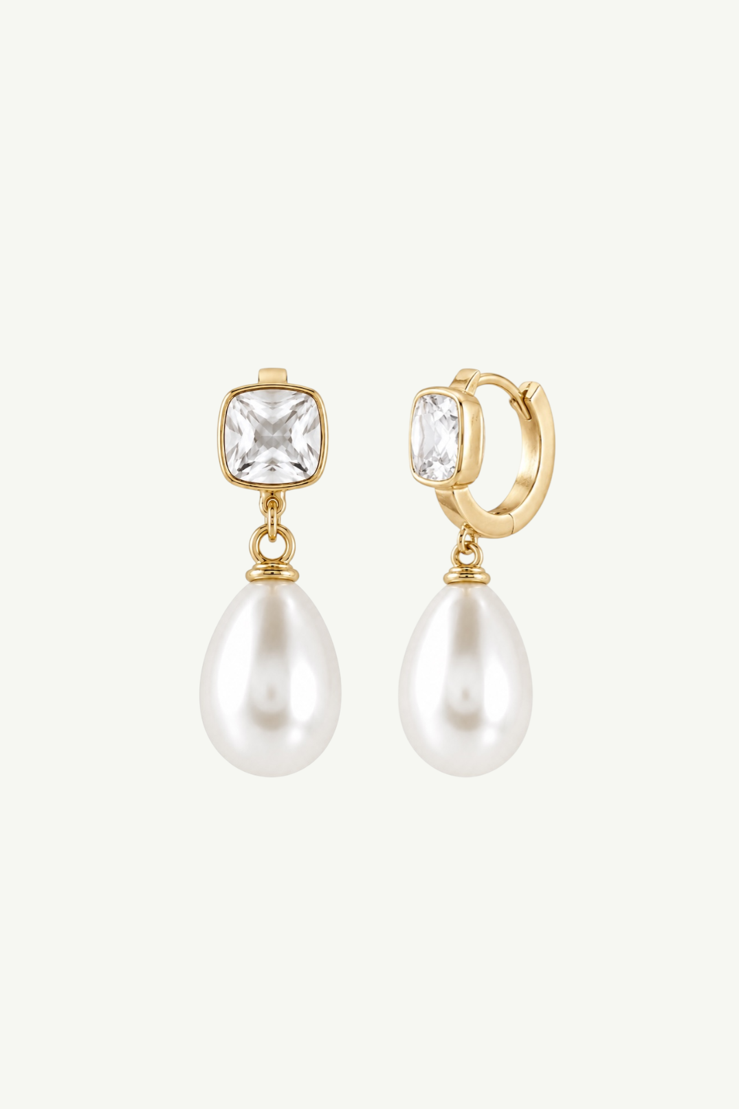A pair of gold huggie hoop earrings with a square clear crystal and a dangling teardrop-shaped white pearl, shown against a light off-white background.