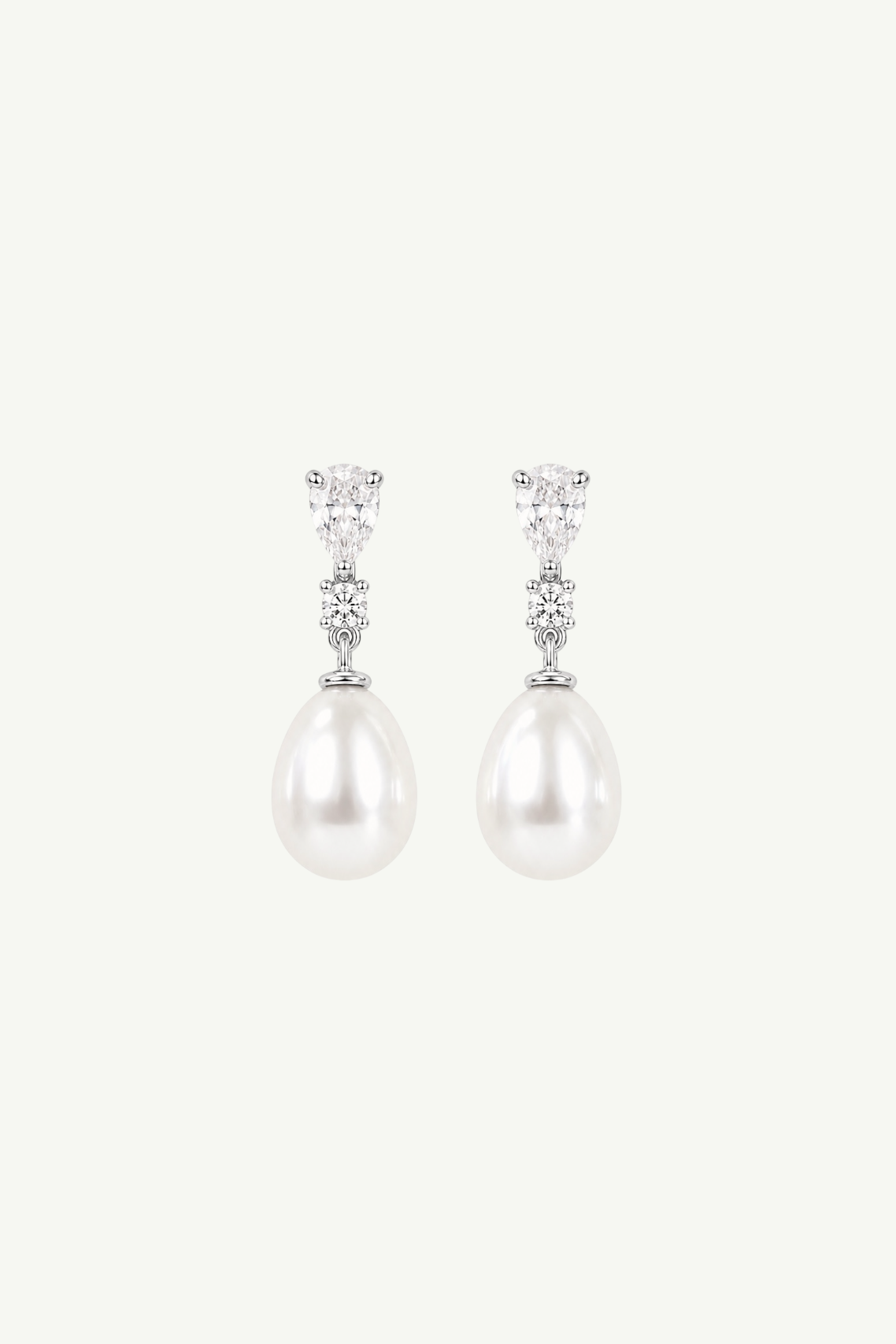 A pair of silver drop earrings featuring a small cluster of clear stones at the top and a large, lustrous white pearl teardrop-shaped drop below, set against a solid off-white background.
